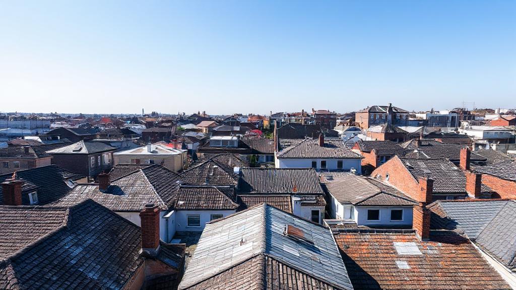 Aerial view of a variety of rooftops in different stages of wear and repair under a clear blue sky.